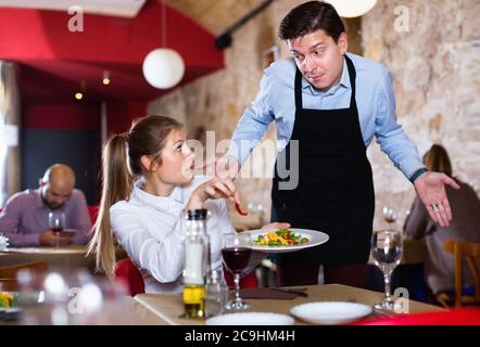 Unzufrieden unzufrieden aggressive junge Frau im Konflikt mit apologetischen Kellner wegen der schlechten Qualität der Speisen im Restaurant Stockfoto