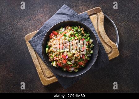 Gekochter Vollkorngetreide Dinkelsalat mit saisonalem Gemüse in einer Schüssel auf braunem Hintergrund. Stockfoto