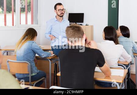 Junger Mann Lehrer gibt interessante Vorlesung für Schüler im Klassenzimmer Stockfoto