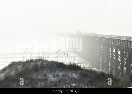 Nebel rollt am Strand und über Pier Stockfoto