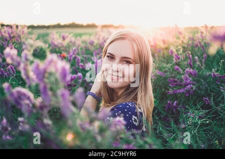 Lächelndes Mädchen geht auf hohem Gras mit lila Blumen überwuchert Stockfoto