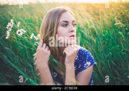 Mädchen sitzen im hohen Gras. Ein Strauß Gänseblümchen in der Hand. Stockfoto