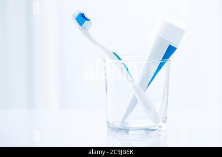 Zahnbürste und Zahnpasta in Glas vor einem schlichten Hintergrund. Stockfoto