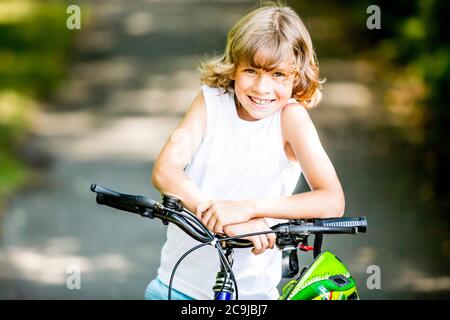 Junge sitzt auf dem Fahrrad im Park, lächelnd, Porträt. Stockfoto