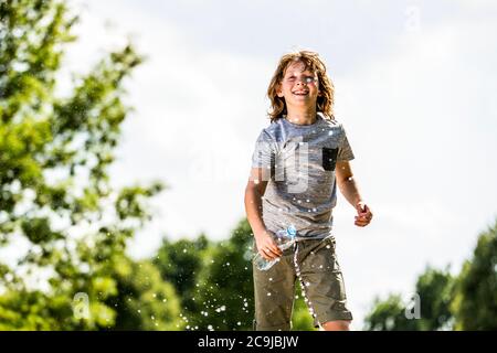 Junge spritzt Wasser aus Plastikflasche, lächelnd, Porträt. Stockfoto
