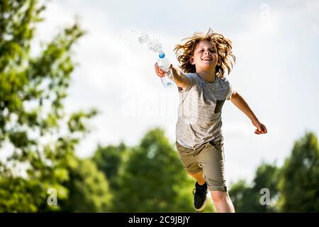 Junge spritzt Wasser aus Plastikflasche, lächelnd, Porträt. Stockfoto