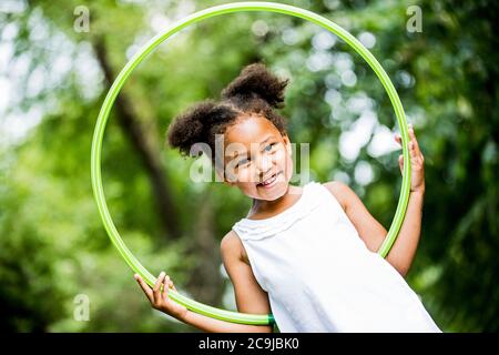 Mädchen spielt mit Hula Hoop im Park, lächelnd, Porträt. Stockfoto