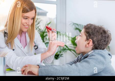 Kinderarzt untersucht die Kehle des Jungen mit einer Stiftlampe und einem Zungenverdichter. Stockfoto
