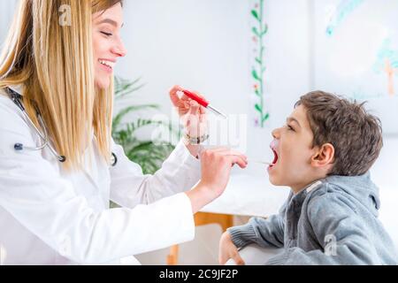 Kinderarzt untersucht die Kehle des Jungen mit einer Stiftlampe und einem Zungenverdichter. Stockfoto