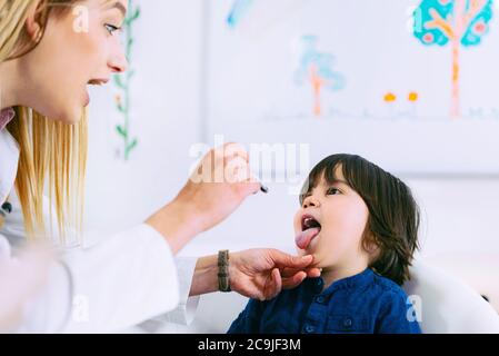 Kinderarzt untersucht die Kehle des Jungen mit einer Taschenlampe. Stockfoto