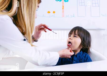 Kinderarzt untersucht die Kehle des Jungen mit einer Taschenlampe. Stockfoto
