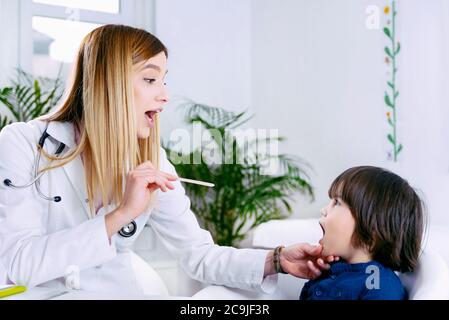 Kinderarzt untersucht die Kehle des Jungen mit Holzzungenverdichter. Stockfoto