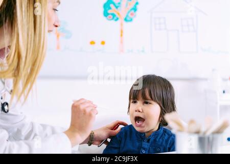 Kinderarzt untersucht die Kehle des Jungen mit Holzzungenverdichter. Stockfoto