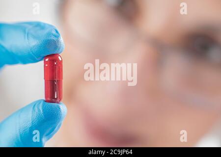 Wissenschaftlerin hält rote Pille mit blauen Handschuhen im Labor. Neue Pille Forschungskonzept. Stockfoto