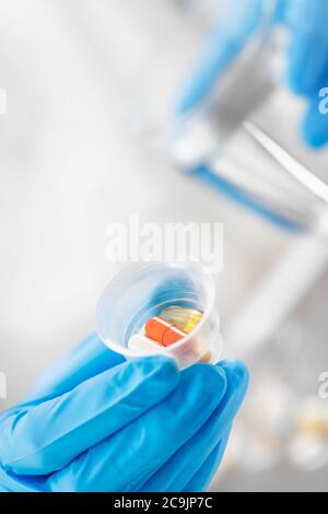 Ärztin Hand in blauen Handschuh hält graduierte Medizin Tasse voller Pillen und Glas Wasser. Stockfoto
