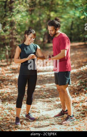 Junges Paar, das nach dem Training im Freien Fortschritte auf ihren smarten Uhren überprüft. Stockfoto