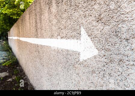 Pfeil mit einer weißen Linie auf einer Steinwand mit negativem Raum und Kopierraum gemalt, um die Richtung anzuzeigen. Stockfoto