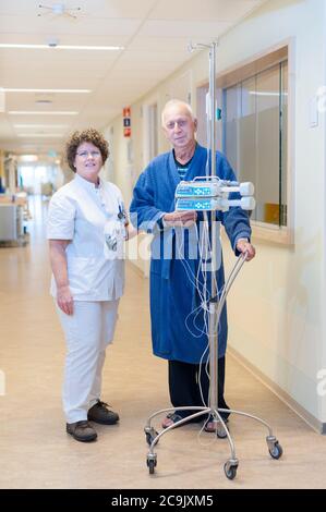 Krankenschwester und Patient, die mit Infusionsständer durch den Flur gehen. Stockfoto
