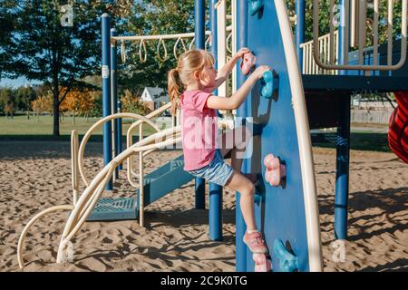 Kleine Vorschulmädchen Klettern Felswand auf Spielplatz draußen am Sommertag. Happy Childhood Lifestyle Konzept. Saisonale Aktivitäten im Freien für Kinder. Stockfoto