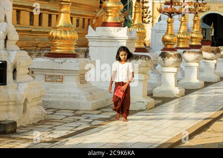 Bagan/Myanmar - 4. Oktober 2019: Ein burmesisches Mädchen läuft auf einem Bürgersteig, der mit burmesischen Skulpturen in einem Tempel geschmückt ist. Stockfoto