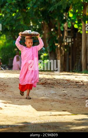 Bagan/Myanmar - 4. Oktober 2019: Eine burmesische Novizenin geht morgens, um Essen zu spenden, indem sie einen Korb auf den Kopf legt. Stockfoto