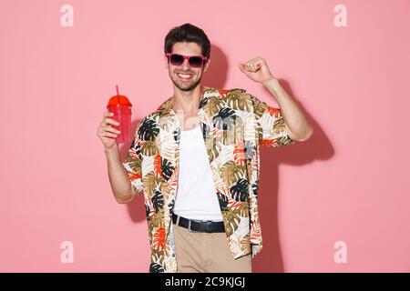 Portrait von fröhlichen kaukasischen Mann in Sonnenbrillen tanzen, während trinken Soda isoliert auf rosa Hintergrund Stockfoto