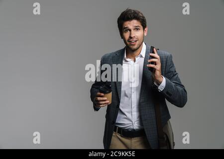 Foto von aufgeregt zuversichtlich Geschäftsmann trinken Kaffee zum Mitnehmen und mit Handy isoliert über graue Wand Stockfoto
