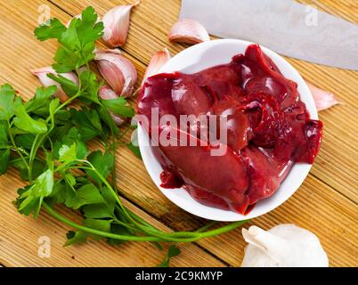 Zutaten zum Kochen. Rohe Kaninchenleber mit Zwiebel, Knoblauch, Gewürzen und Kräutern auf Holztisch Stockfoto
