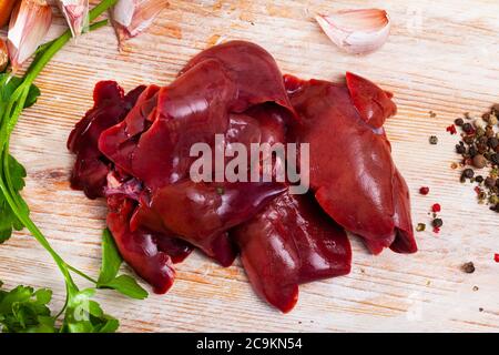 Frische rohe Kaninchenleber mit Gewürzen auf Holzgrund. Diätetisches Fleischprodukt Stockfoto