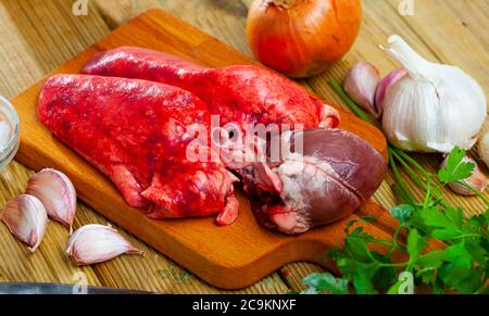 Frische Hammelfleisch, Lunge und Herz, auf Holzgrund mit Petersilie, Knoblauch und Zwiebel Stockfoto