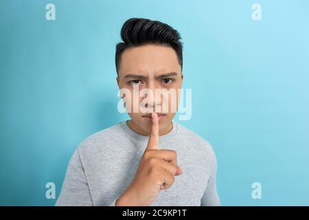 Serious gut aussehende Männchen hält Vorderfinger auf den Lippen, versucht Verschwörung zu halten, schaut beiseite, sagt: Shh, machen Sie Schweigen bitte. Stockfoto