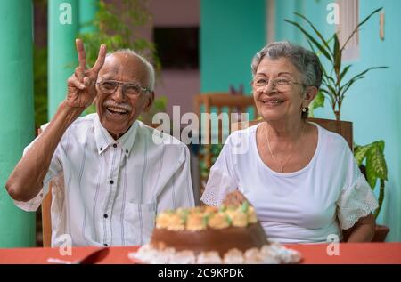 Lächelndes, älteres Paar, das vor einem Kuchen sitzt Stockfoto