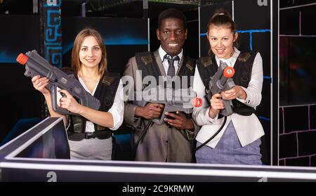 Afrikanische Mann und zwei jungen kaukasischen Frauen holding Laser Gewehren und auf der Laser tag Zimmer posing Stockfoto