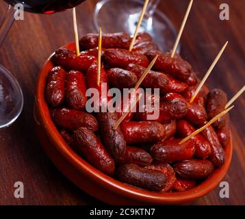 Heiße Mini-Chorizo-Würstchen in Keramikschale serviert. Beliebte spanische Vorspeise für Rotwein Stockfoto