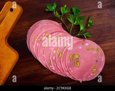Bild von Mortadela-Wurst mit in Scheiben geschnittenen Oliven auf Holzschreibtisch, Nahaufnahme Stockfoto