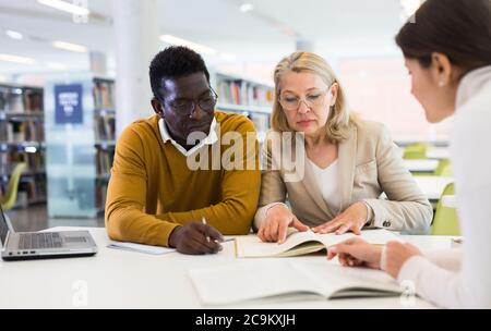 Tutorin hilft Studenten, die sich auf die Prüfung in der Bibliothek vorbereiten Stockfoto