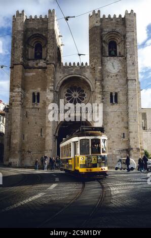 LISSABON, PORTUGAL - 2. FEBRUAR 2019: Traditionelle gelbe elektrische Straßenbahn vor der mittelalterlichen Kathedrale von Lissabon, Portugal, mit Touristen Stockfoto