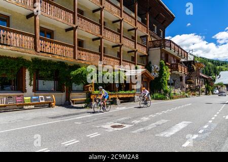 Radfahrer steigen vom Col de Vars und durch ein alpines Dorf mit typischen Holzhäusern. Vars, Hautes-Alpes, Frankreich, Juli 2020 Stockfoto