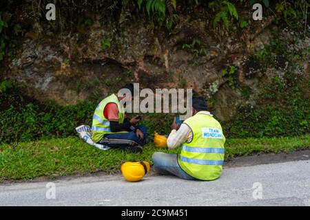 Straßenreparatur in Asien. Eingezäunter Straßenabschnitt mit Grube. Arbeiter in Overalls ruhen am Rande, Mittagspause Stockfoto