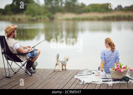 Ehepartner genießen Angeln und ein Picknick mit ihrem Hund an einem schönen Tag Stockfoto