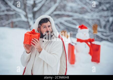 Winter Portrait von schönen Hipster im Schnee Garten mit Geschenk machen Schneemann. Weihnachtsmann und Schneemann auf weißem Schnee Hintergrund. Santa betrunken zu Hause. Stockfoto