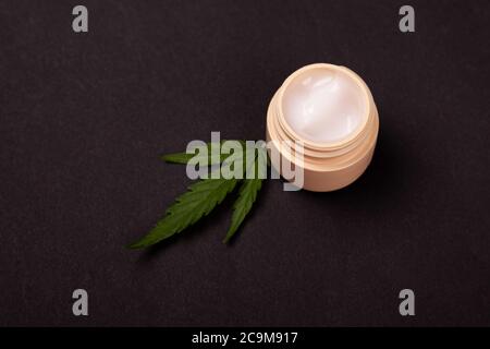 Schönheit, Hautpflege-Kosmetik mit Marihuana-Extrakt. Verjüngende Handcreme mit medizinischen Cannabispflanze Blatt auf schwarzem Hintergrund. Stockfoto