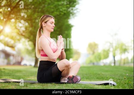 Zen Yoga Frau lotos Position auf dem Gras. Weibliche sitzende in Meditation Pose im Freien mit den Händen in namaste. Mädchen meditiert auf Matte in der Natur Stockfoto