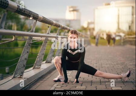 Sportlerin Frau in Fitness-Kleidung macht Stretching exersice im öffentlichen Park vor dem Training oder Laufen und Musik hören Stockfoto