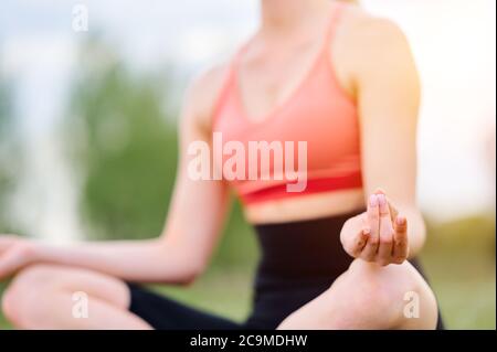 Junge Frau sitzt in Lotos Pose im Sommer Park auf Gras. Frau praktiziert Meditation in Yoga-Halle nach harten Tag Stockfoto