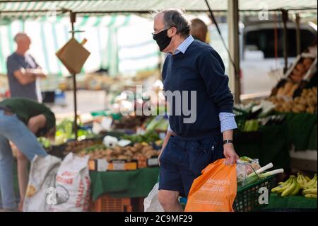 Richmond, North Yorkshire, Großbritannien - 1. August 2020: Ein reifer Mann mit einer schützenden Gesichtsmaske trägt Shopping auf einem Outdoor-Markt Stockfoto