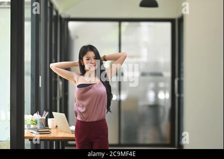 Eine schöne Frau streckt ihren Arm und entspannt sich am Arbeitstisch. Stockfoto