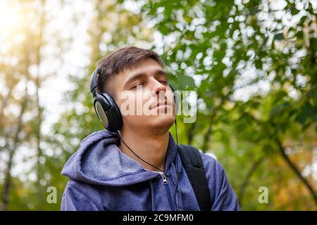 Junger Mann in Kopfhörern lauscht der Musik im Park Stockfoto