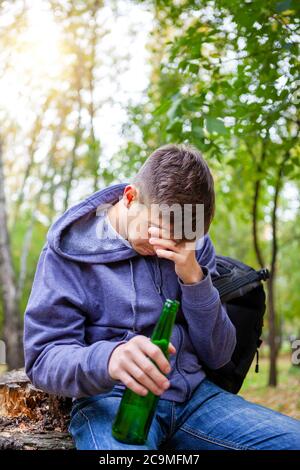 Trauriger junger Mann mit einer Flasche Bier im Park Stockfoto