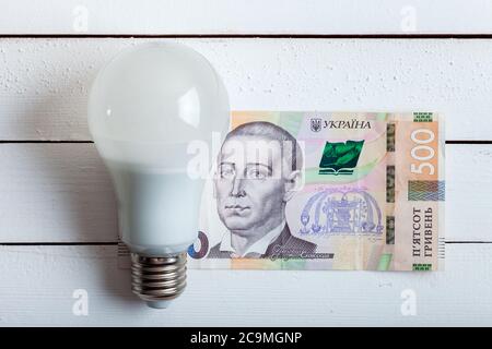 led-Lampe mit Geld liegt auf einem weißen Holztisch von Bord. Stockfoto